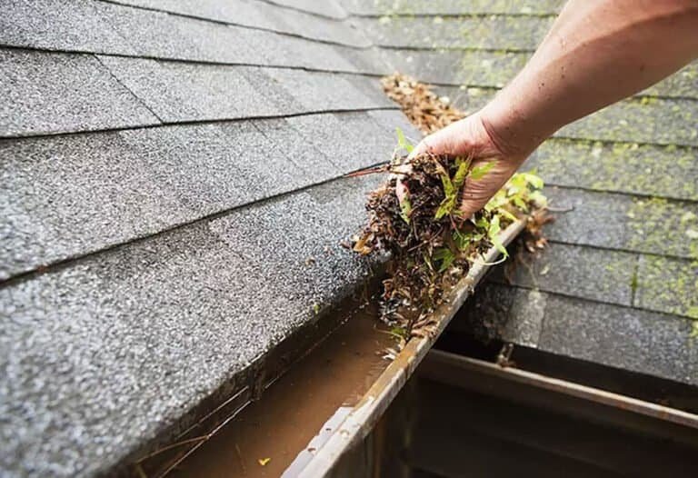 Hand clearing leaves out of a roof gutter